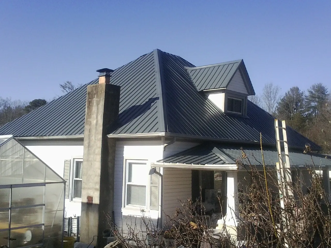 Dark blue standing seam metal roof on a white farmhouse with dormer — Slate & Tile Roof Repair by Roofing Brothers in Angelus Oaks