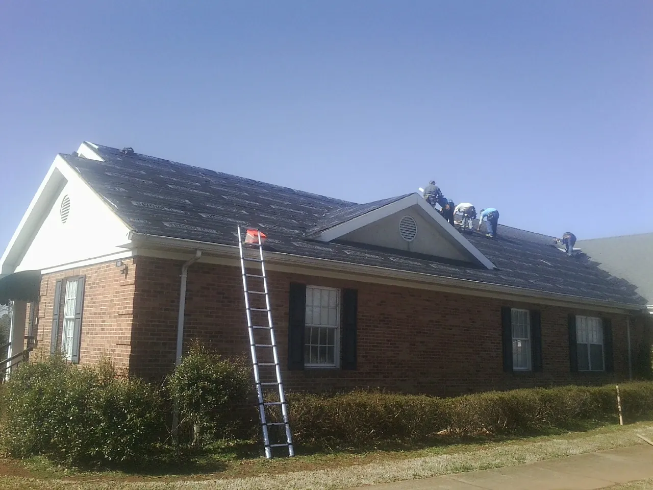 Crew tearing shingles off a brick ranch roof with a ladder set — Emergency Roof Repair work by our crew in Angelus Oaks