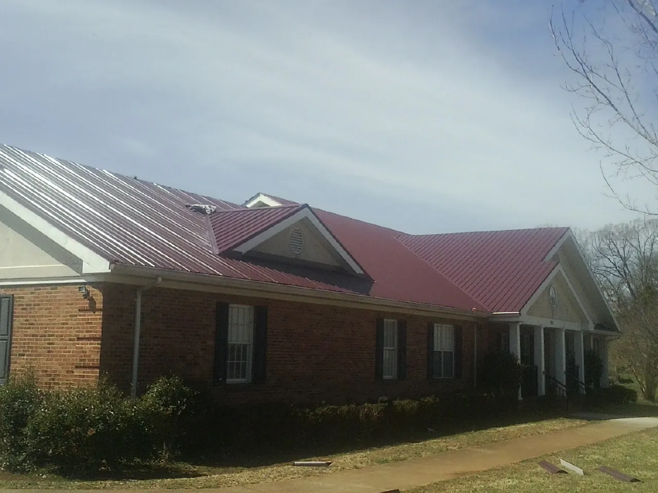 Red metal roof with gabled entries on a long brick building, from a Hail Damage Roof Repair job in Angelus Oaks