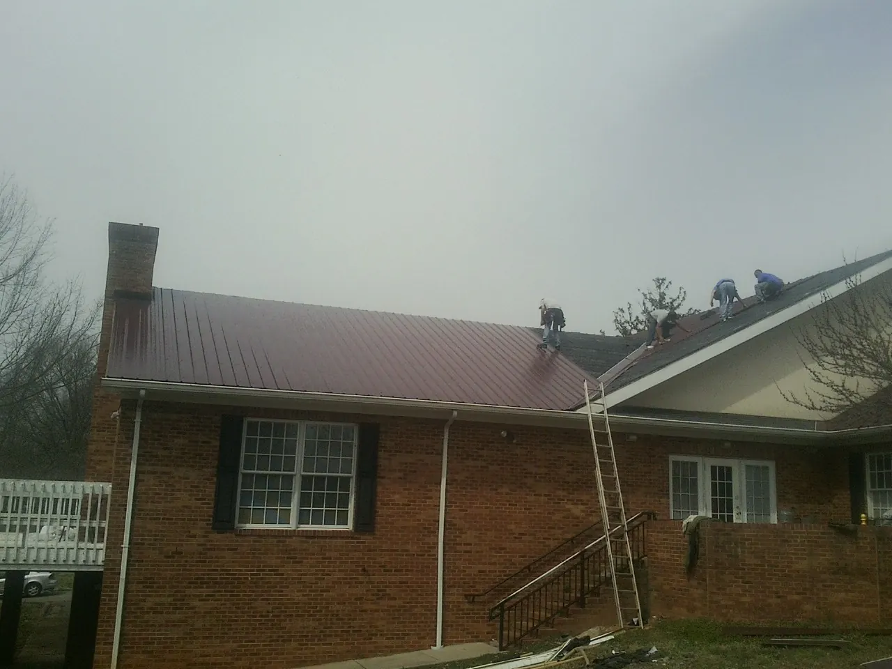 Crew setting red metal roofing panels on a brick home in Angelus Oaks