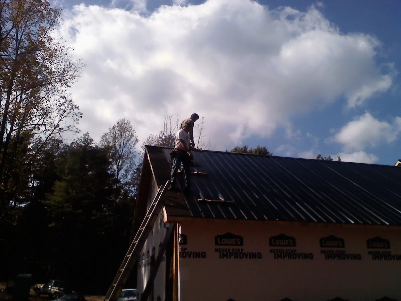 Roofer fastening dark metal panels high against a cloudy sky, from a Roof Inspection job in Angelus Oaks