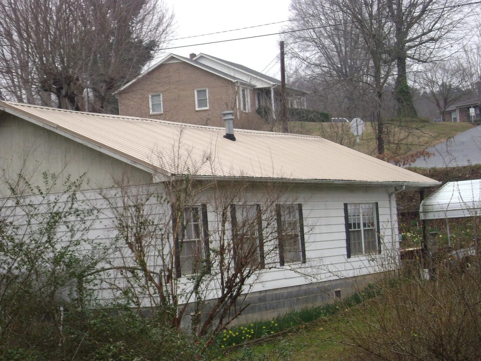 Tan metal roof on a white sided house set into a hillside — Commercial Roofing by Roofing Brothers in Angelus Oaks