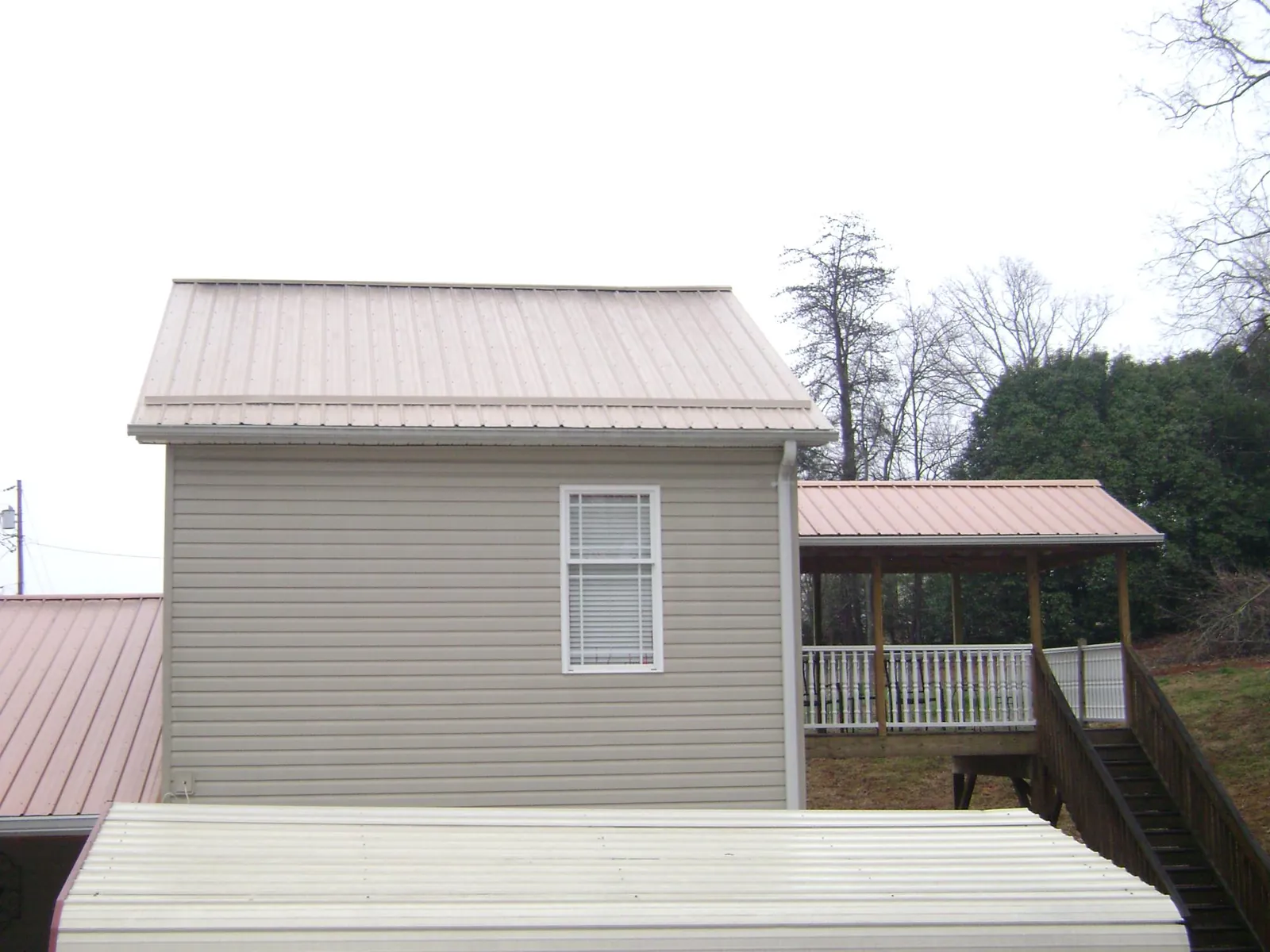 Tan metal roofs on a two story addition and attached porch, from a Roof Replacement job in Angelus Oaks